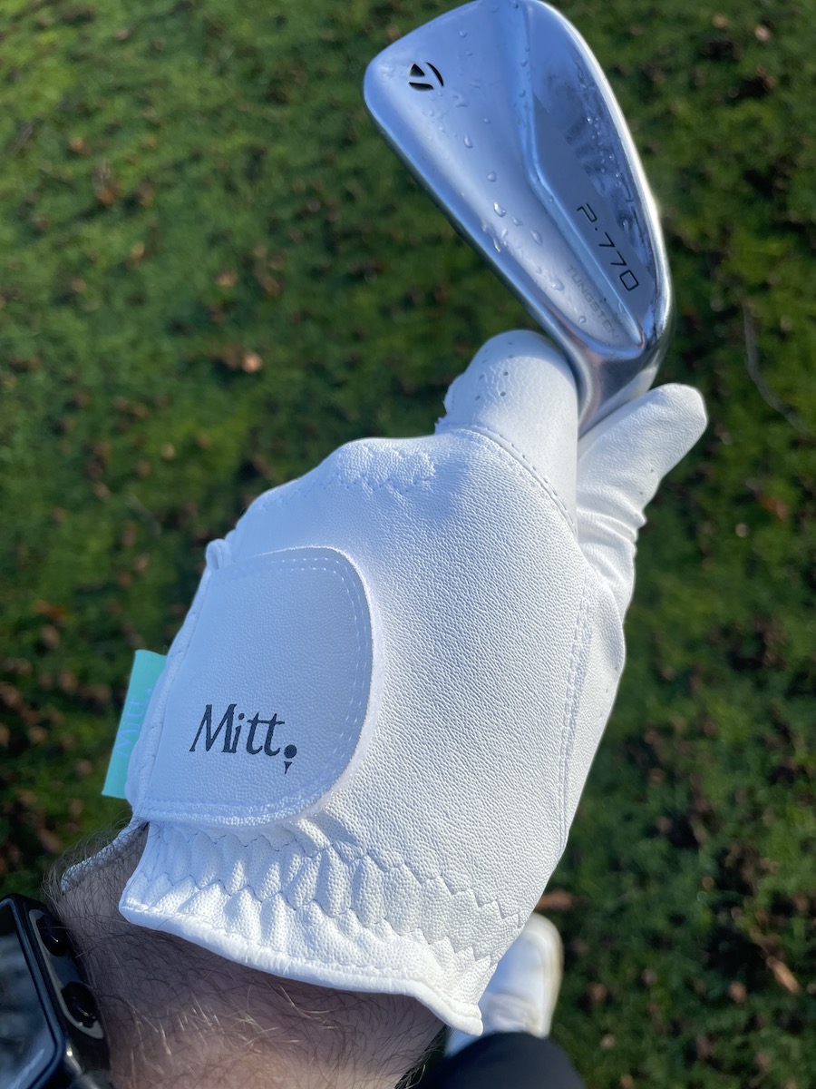 Mitt Golf glove being worn on the left hand whilst holding a TaylorMade P770 iron.