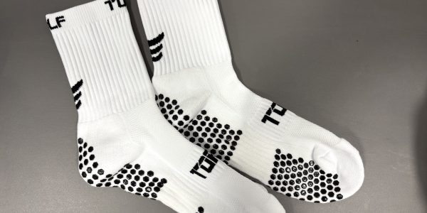 Pair of white Torn golf socks with grey spots on a grey background.