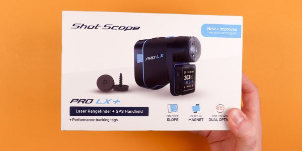A hand holding the box of the Shot Scope PRO LX+ laser rangefinder against an orange background